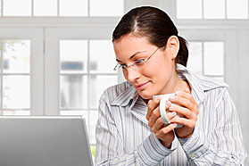 A woman with coffee looking at a laptop.